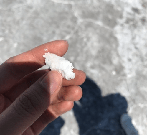A hand holding a small piece of white salt on a light-colored surface.