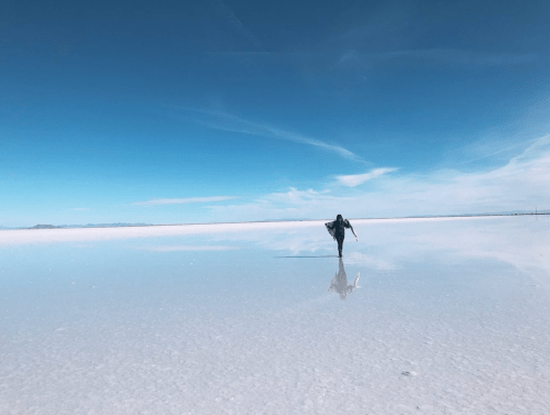 A person walks on a vast, reflective salt flat under a clear blue sky.