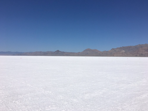 A vast, flat expanse of white salt flats under a clear blue sky, with distant mountains on the horizon.
