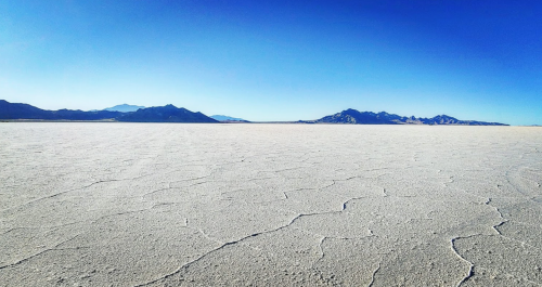 A vast, cracked salt flat stretches towards distant mountains under a clear blue sky.