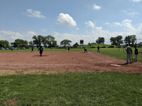 A sunny day at a baseball field with players in action on the diamond and green grass surrounding the area.