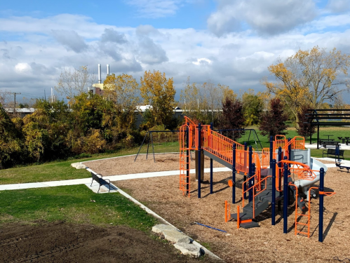 A colorful playground with orange equipment surrounded by trees and a cloudy sky in the background.