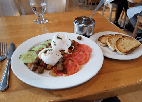 A plate of poached eggs on vegetables and diced meat, served with toast on the side. Water glass in the background.
