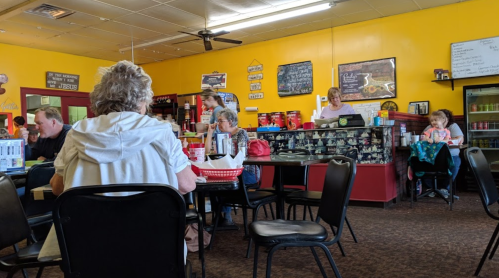A cozy diner with patrons seated at tables, colorful walls, and a counter with a server attending to customers.