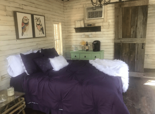 Cozy bedroom with a purple bedspread, wooden walls, and a green dresser, featuring artwork and an air conditioner.