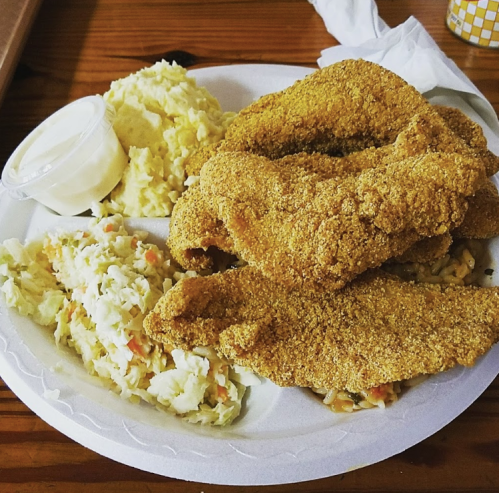 A plate of crispy fried fish fillets, creamy mashed potatoes, and coleslaw, served with a side of dipping sauce.