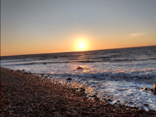Sunset over the ocean, with waves gently lapping against a rocky shore, creating a serene coastal scene.