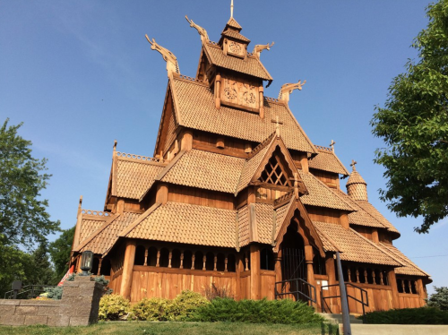 A wooden church with intricate carvings and a steeply pitched roof, featuring dragon sculptures and surrounded by greenery.