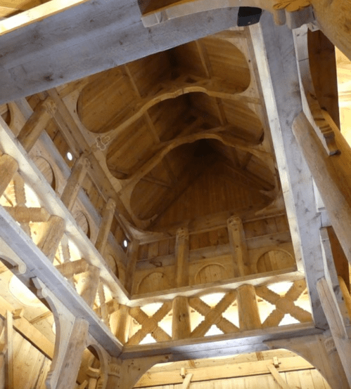 Interior view of a wooden structure, showcasing intricate beams and a high, vaulted ceiling.