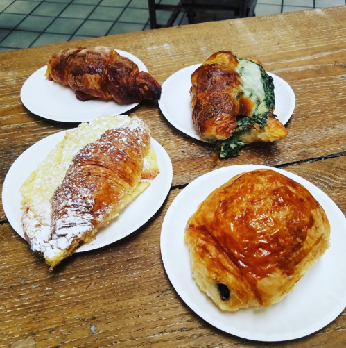Four pastries on paper plates: a croissant, a sweet pastry, a spinach-filled pastry, and a chocolate croissant.