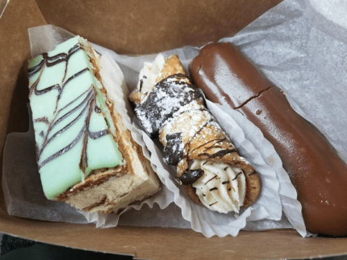 A box containing three desserts: a mint-striped cake, a chocolate-covered cannoli, and a chocolate eclair.