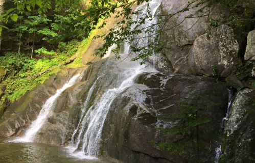 A serene waterfall cascading over rocky terrain, surrounded by lush green foliage.