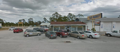 A small fish market with several parked cars outside, set against a cloudy sky and surrounded by trees.