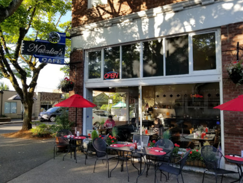 Exterior of Natalie's Café with outdoor seating, red umbrellas, and an "Open" sign in the window.