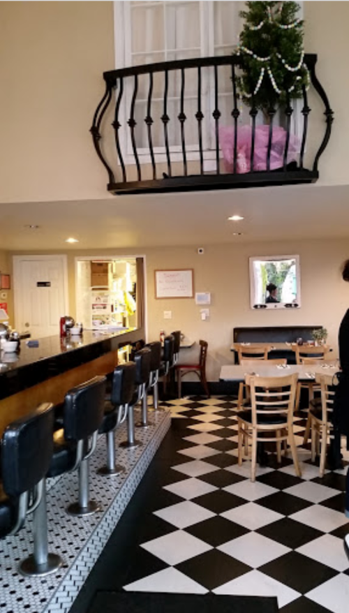 Interior of a cozy café featuring a black and white checkered floor, bar seating, and a balcony decorated for the holidays.
