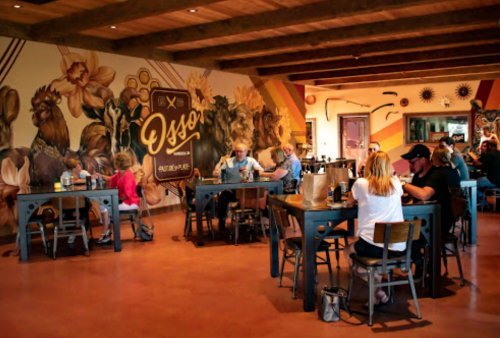 A cozy restaurant interior with patrons dining at tables, featuring a colorful mural of flowers and animals on the wall.