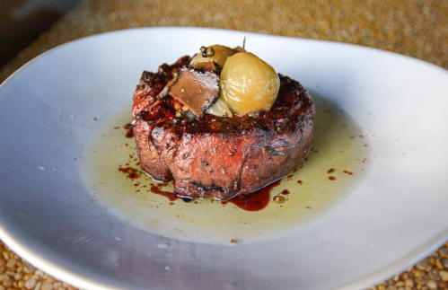 A beautifully plated round steak topped with mushrooms and a whole onion, drizzled with a rich sauce.