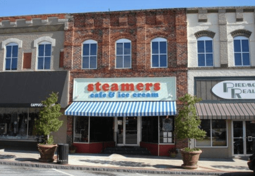 A storefront with a sign reading "Steamers Cafe & Ice Cream," featuring a striped awning and potted plants outside.