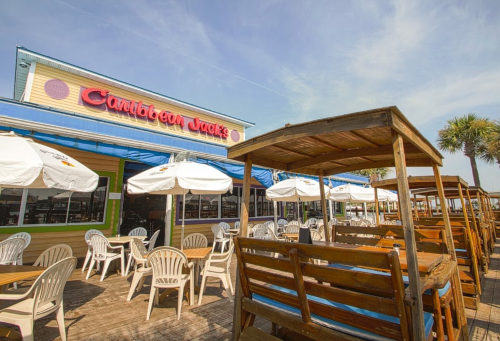 Outdoor seating area of Caribbean Jack's restaurant with umbrellas and wooden tables, set against a sunny sky.