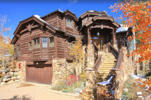 A large, rustic wooden house with stone accents, featuring a grand entrance and autumn foliage.