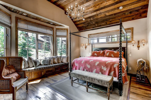 Cozy bedroom with a four-poster bed, wooden beams, large windows, and a seating area by the window.