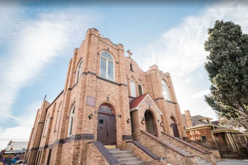 A large brick church with arched windows and a steep staircase, set against a clear blue sky.