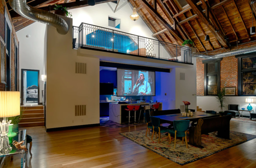 Spacious loft with high ceilings, modern decor, and a large screen displaying a man playing an instrument.