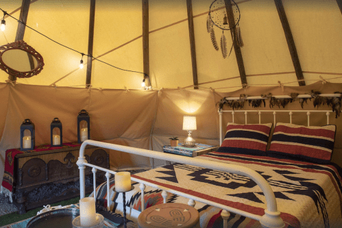 Cozy tent interior with a bed, decorative blankets, lanterns, and a wooden chest, creating a warm, inviting atmosphere.