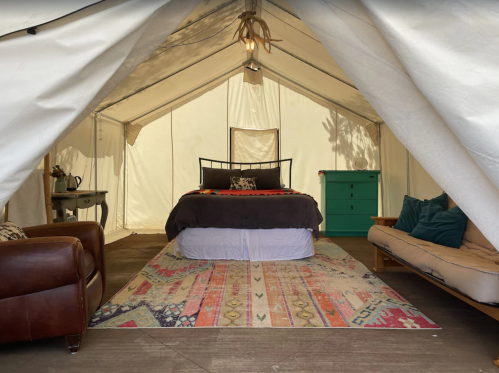 Cozy tent interior with a bed, colorful rug, couch, and decorative furnishings. Warm, inviting atmosphere.