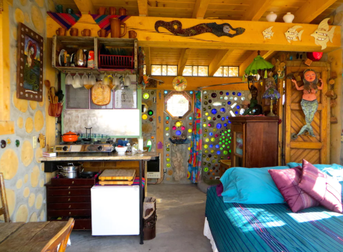 Cozy interior of a colorful cottage with a kitchen, vibrant decor, and a bed, featuring unique artistic elements.