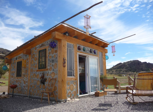 A small, rustic house made of stone and wood, surrounded by a scenic landscape and decorated with colorful lanterns.