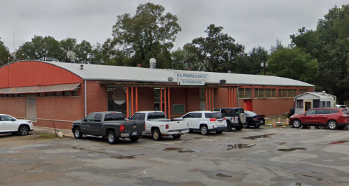 A brick building with a metal roof, featuring parked vehicles and a sign that reads "R. A. Porras & Sons Co."