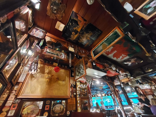 A cozy restaurant interior with wooden walls, vintage decor, mirrors, and colorful artwork hanging from the ceiling.