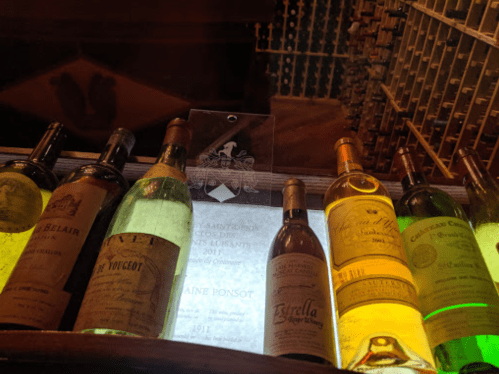 A display of various wine bottles, including reds and whites, with a plaque in the center highlighting a vintage.
