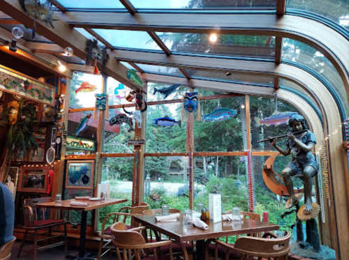 Interior of a cozy restaurant with large windows, wooden decor, colorful fish art, and a statue of a musician.
