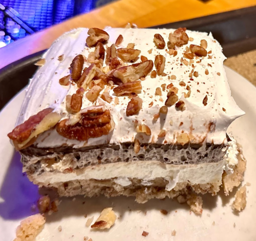A slice of layered dessert topped with whipped cream and chopped pecans on a plate.