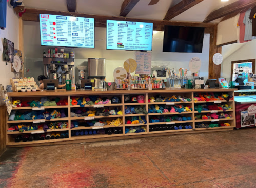 A colorful display of hats and drinks at a counter with menus and a large screen in a cozy shop interior.