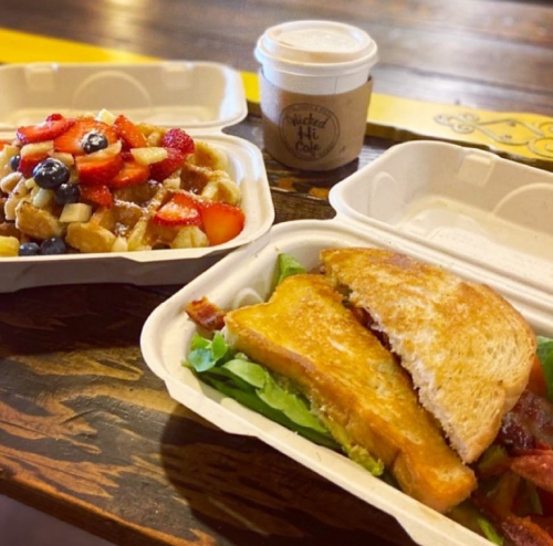 A sandwich with bacon and lettuce, a fruit salad, and a coffee cup on a wooden table.