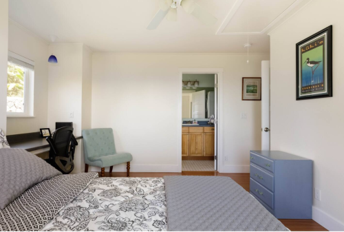 A bright bedroom featuring a bed, a chair, a dresser, and an open door leading to a bathroom.
