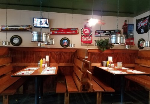 Cozy restaurant interior with wooden booths, racing memorabilia, and a TV, featuring condiments on tables.