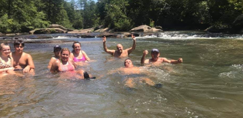 A group of people enjoying a sunny day in a river, some sitting and others floating in the water.