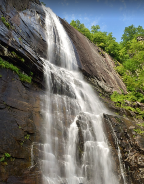 A majestic waterfall cascading down a rocky cliff, surrounded by lush green trees under a clear blue sky.