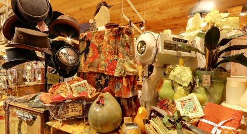 A vintage display featuring hats, fabric, a sewing machine, and decorative items in a cozy shop setting.