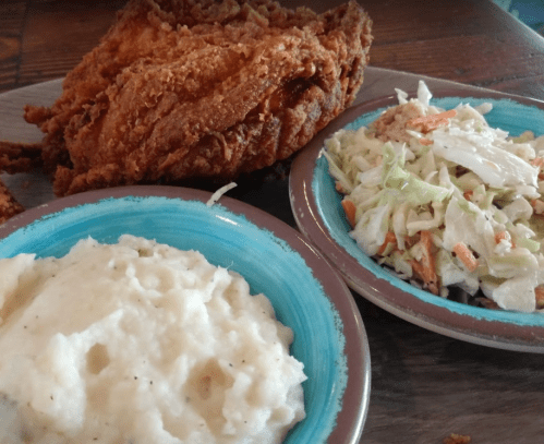 A plate featuring crispy fried chicken, creamy mashed potatoes, and a side of coleslaw in colorful bowls.