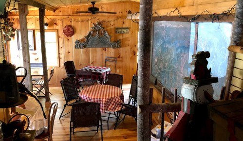 Cozy wooden interior with checkered tables, chairs, and a chalkboard, creating a warm, inviting atmosphere.