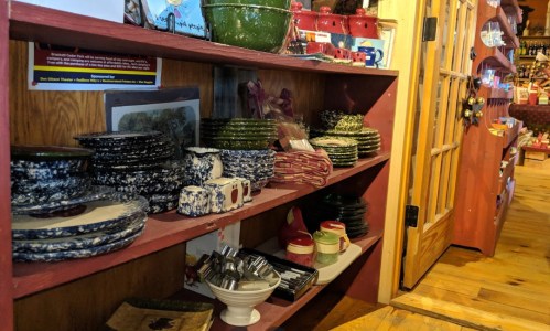 A wooden shelf filled with various colorful dishes, plates, and kitchenware in a cozy store setting.