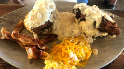 A plate with two biscuit sandwiches topped with gravy, crispy bacon, and a cheesy omelet.