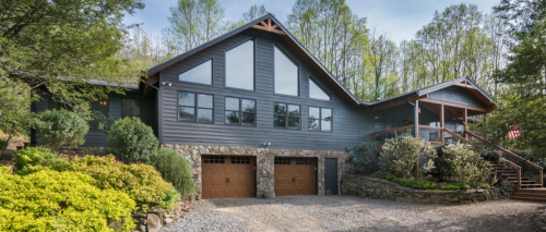 A modern house with large windows, stone accents, and a landscaped yard, surrounded by trees.