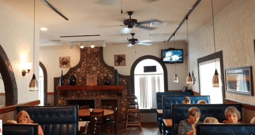 Interior of a restaurant featuring booths, a stone fireplace, and a TV, with diners seated at tables and booths.