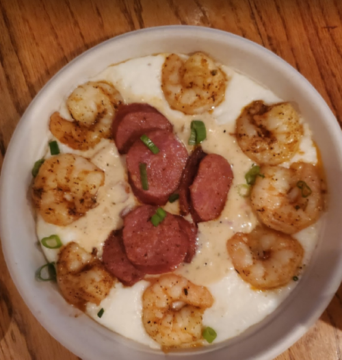 A bowl of creamy grits topped with shrimp, sausage slices, and green onions.